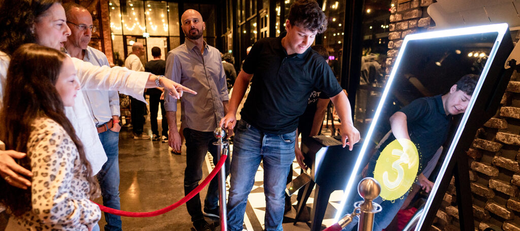 Guests interacting with a mirror photo booth at an evening event venue