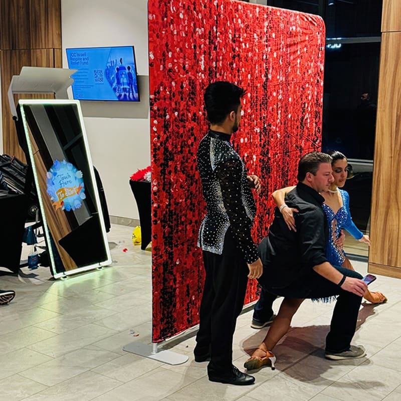 Guests dancing and posing in front of a red sequin photo booth backdrop during an event.