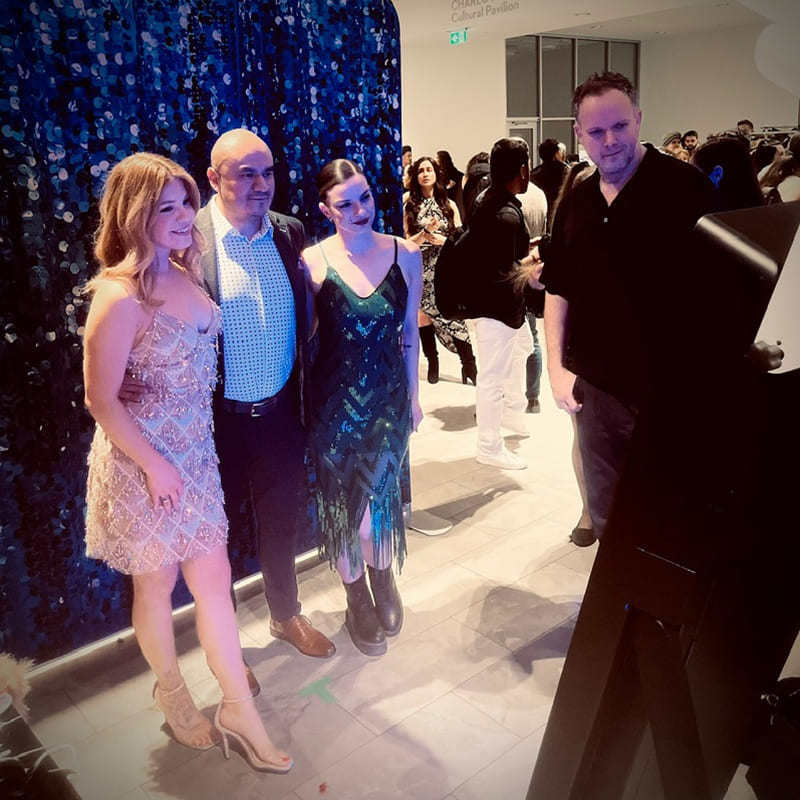 Guests posing for a photo at an event in front of a blue sequin photo booth backdrop.
