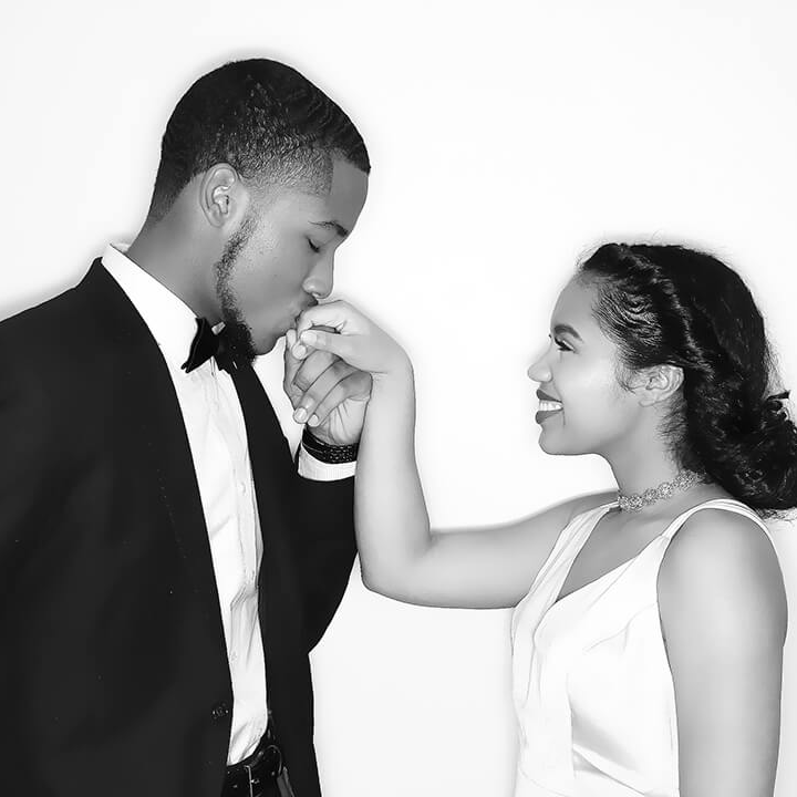 Black and white photo booth portrait of a couple, with one partner kissing the other’s hand in an elegant pose.