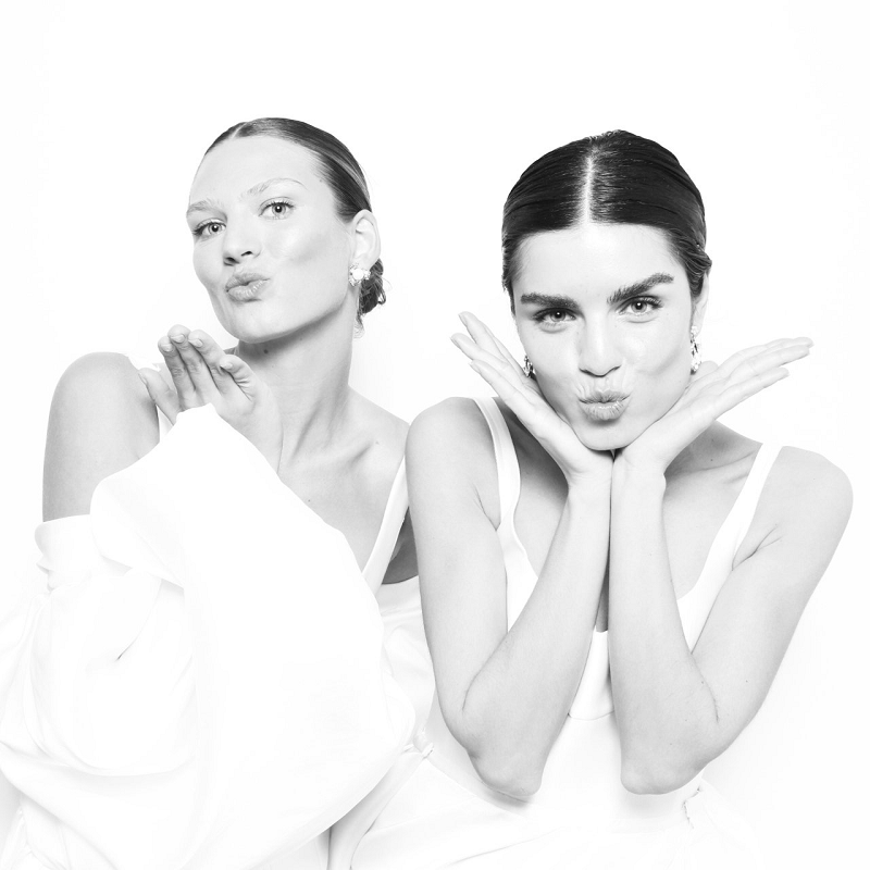 Black and white photo booth portrait of two women posing playfully with puckered lips and expressive hand gestures.