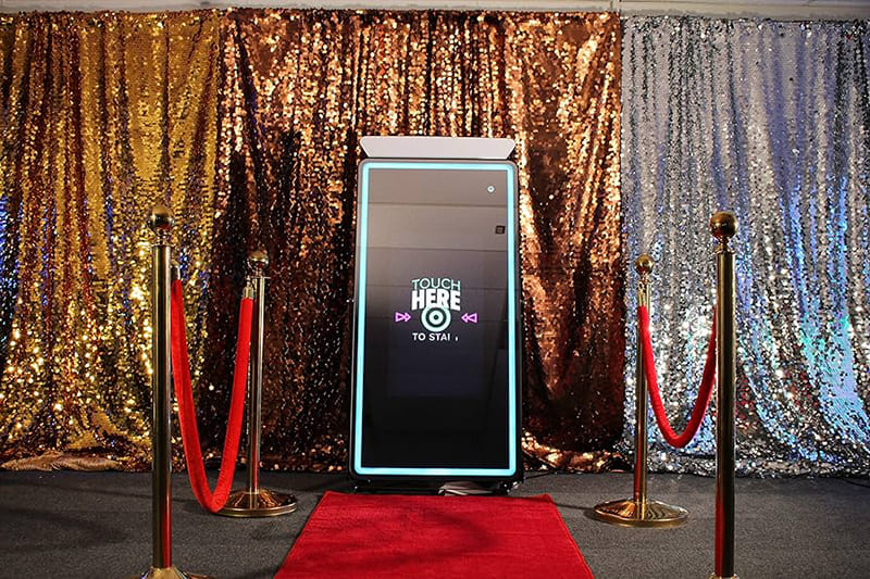 Luxury mirror photo booth set on a red carpet with velvet stanchions and gold and silver sequin backdrops.